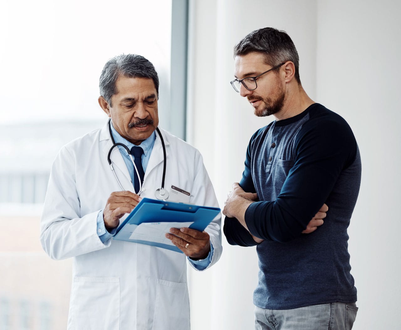 A doctor in a white coat discusses notes with a patient in a casual setting at a hypertension clinic, emphasizing a serious conversation.