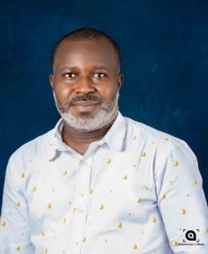 Dr. Atune Bright Maduka wearing a white shirt adorned with yellow banana prints stands against a blue backdrop, exuding a calm demeanor.