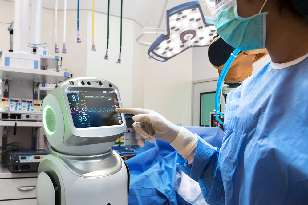 A medical professional in scrubs and gloves interacts with a robotic device displaying vital signs in a surgical environment.