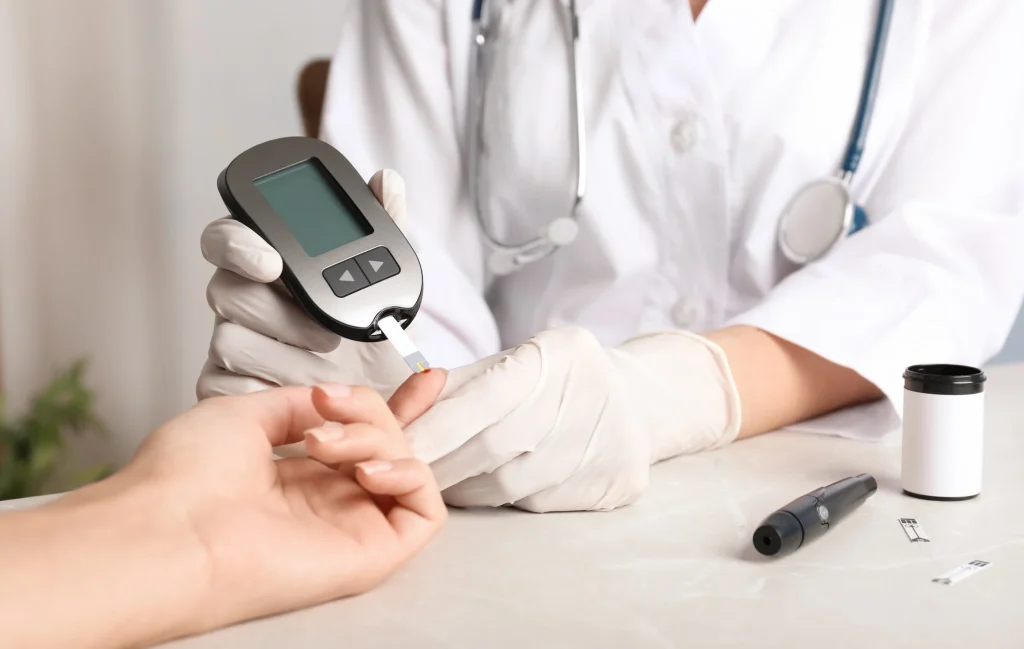 A healthcare professional in gloves measures blood glucose using a glucometer on a patient's hand during a medical consultation.
