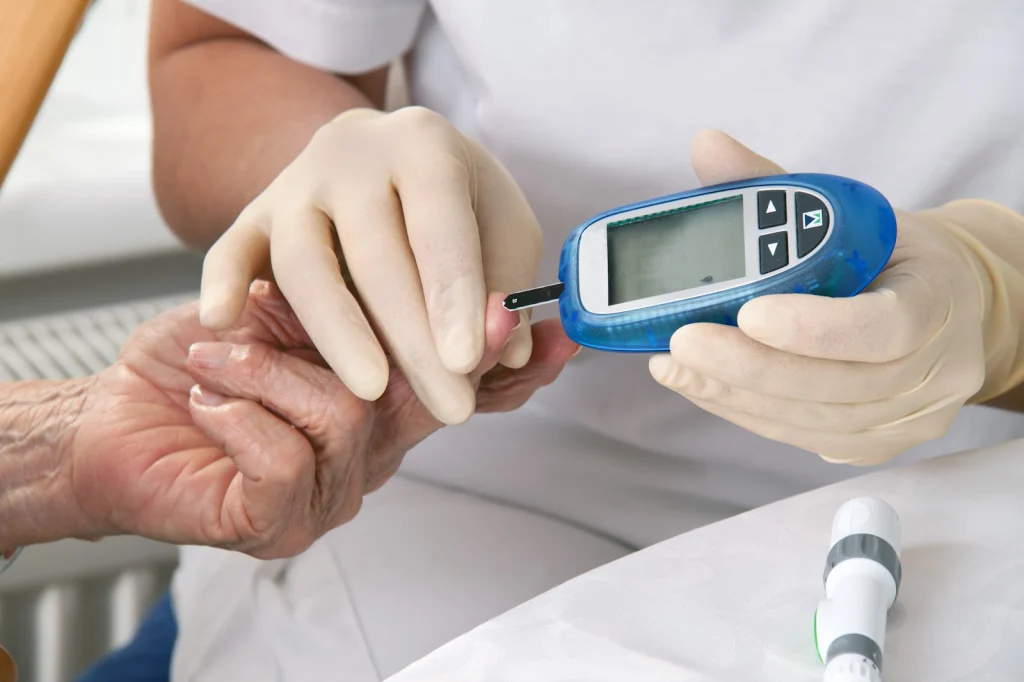 A healthcare professional in gloves checks a patient's blood sugar using a glucometer, focusing on an elderly person's hand.